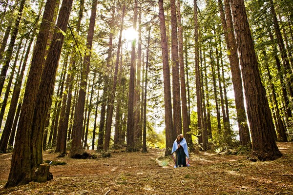 Hispanic couple wrapped in blanket in forest