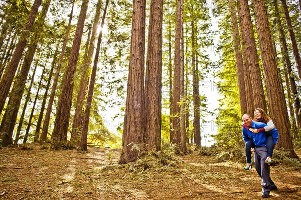 Hispanic man carrying girlfriend piggy back in forest