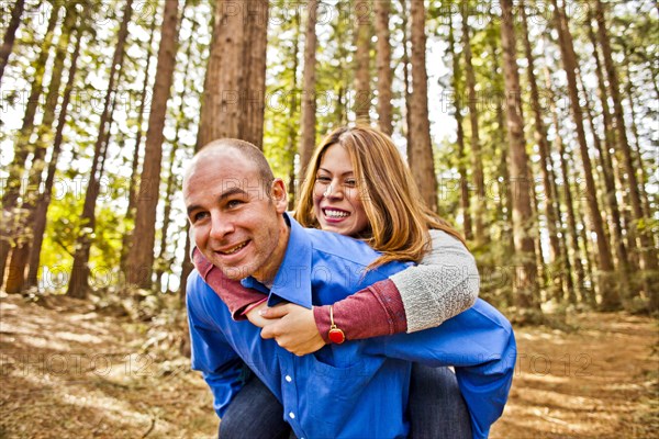 Hispanic man carrying girlfriend piggy back in forest