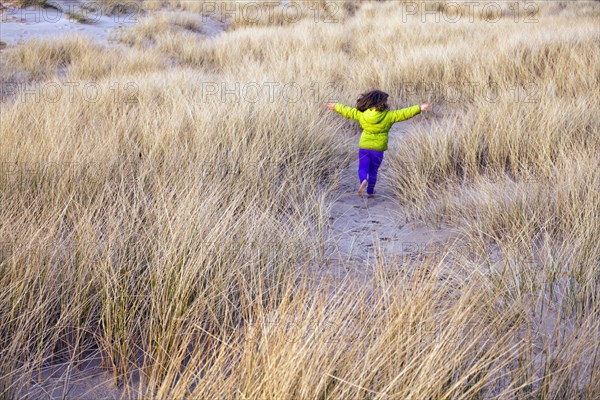 Caucasian girl running in grassy sand dune