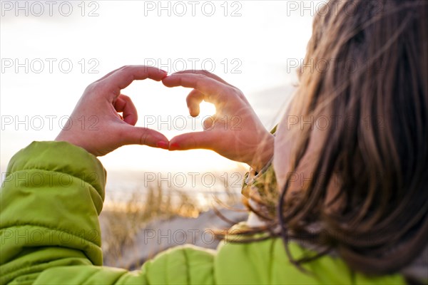 Caucasian girl admiring sunset through hands