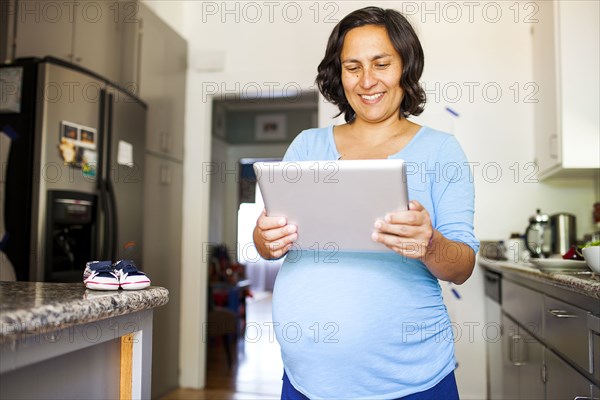 Pregnant Hispanic woman using tablet computer in kitchen