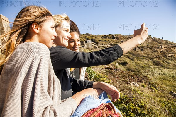 Women taking cell phone picture together on rural hillside