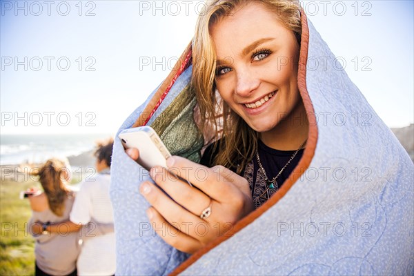 Woman using cell phone in blanket on rural hillside