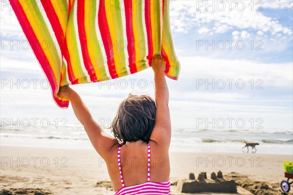 Caucasian woman holding towel in wind on beach