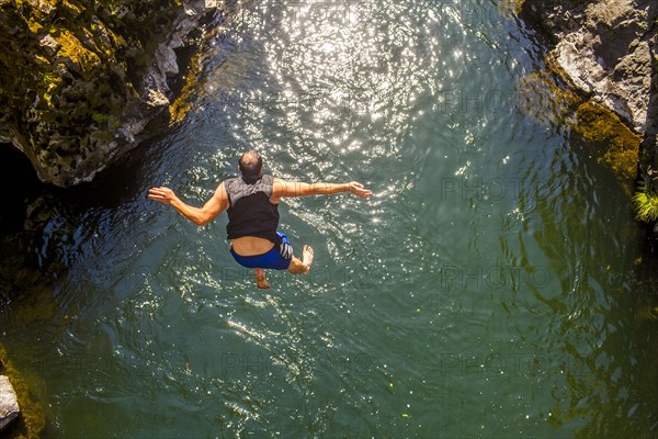 Caucasian man jumping off rocks into ocean