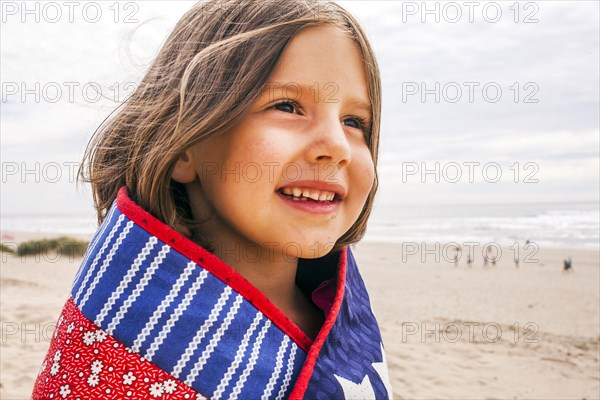 Caucasian girl wrapped in blanket on beach