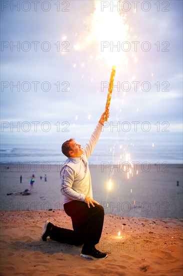 Caucasian man holding fireworks on beach