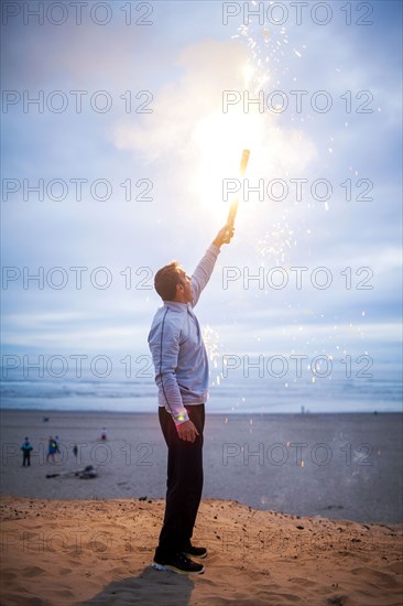 Caucasian man holding fireworks on beach