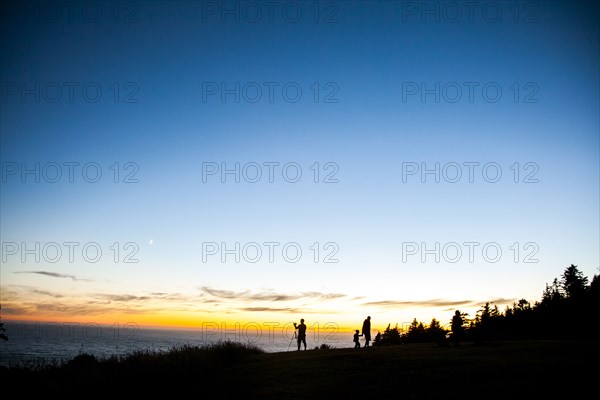 Silhouette of family on rural hillside at sunset