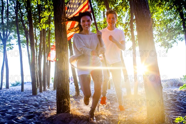 Caucasian couple carrying American flag in trees on beach