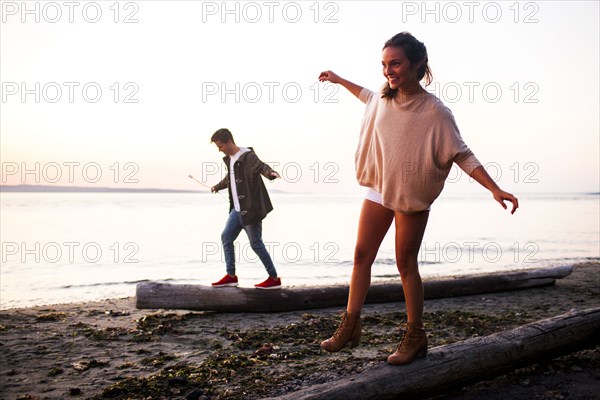 Caucasian couple walking on logs on beach