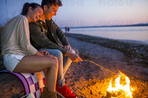 Caucasian couple roasting marshmallows on fire at beach