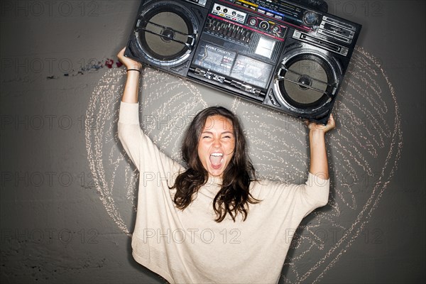 Caucasian woman holding boom box near chalk heart on wall