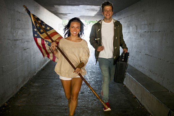 Caucasian couple carrying American flag and boom box in tunnel