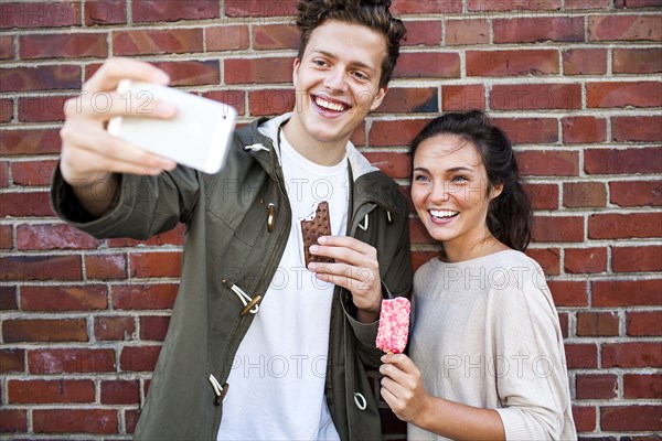 Caucasian couple taking selfie near red brick wall