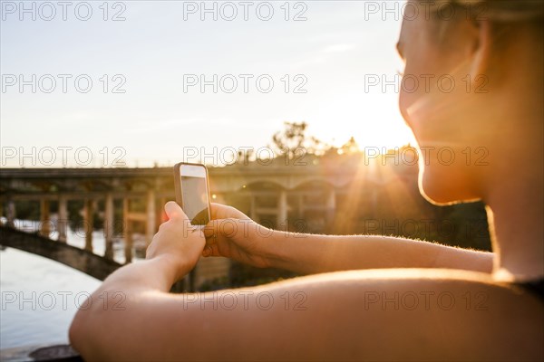 Caucasian teenage girl taking cell phone photograph of bridge