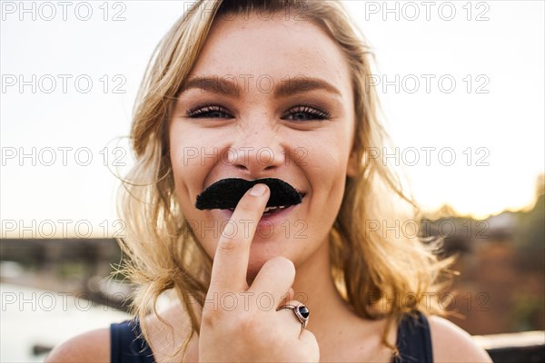 Caucasian teenage girl playing with fake mustache