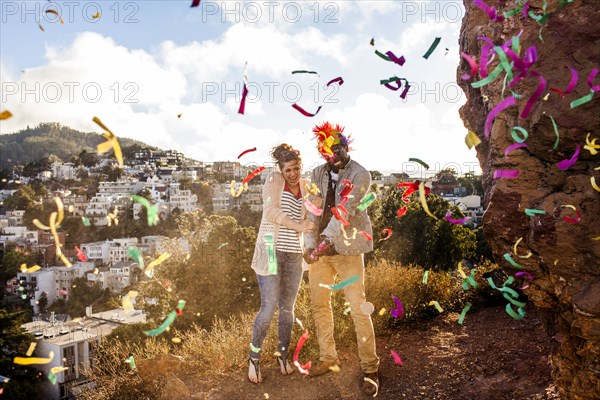 Couple throwing confetti on hill overlooking cityscape