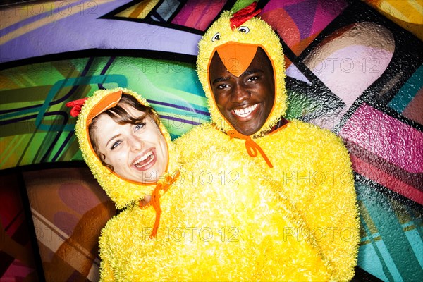 Couple in chicken costumes smiling near graffiti wall