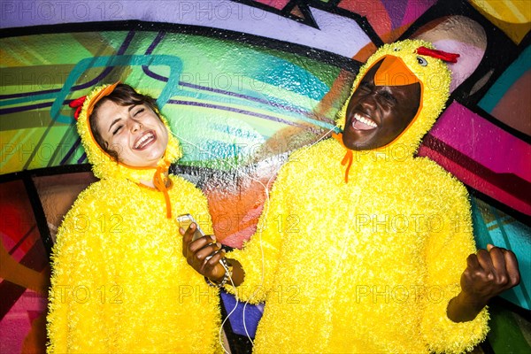 Couple in identical costumes listening to earbuds near graffiti wall