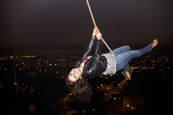 Caucasian woman on rope swinging over scenic view of cityscape