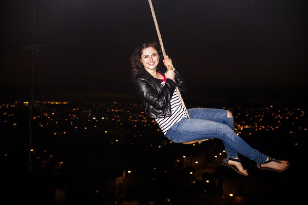 Caucasian woman on rope swinging over scenic view of cityscape