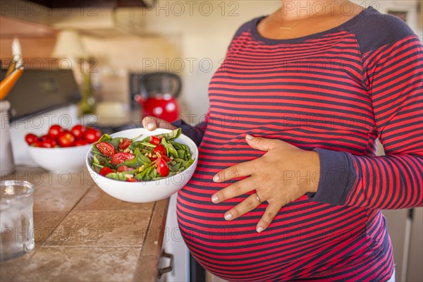 Pregnant Caucasian mother holding salad in kitchen