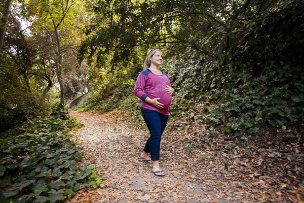 Pregnant Caucasian woman holding her stomach on forest path