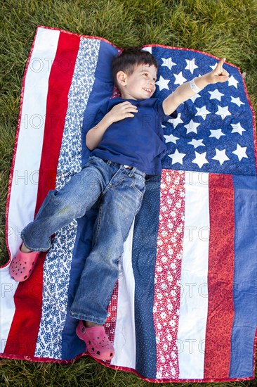 Mixed race boy pointing up on American flag blanket on grass