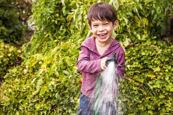 Mixed race boy playing with hose in garden
