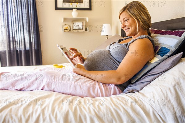 Pregnant Caucasian woman using digital tablet in bed