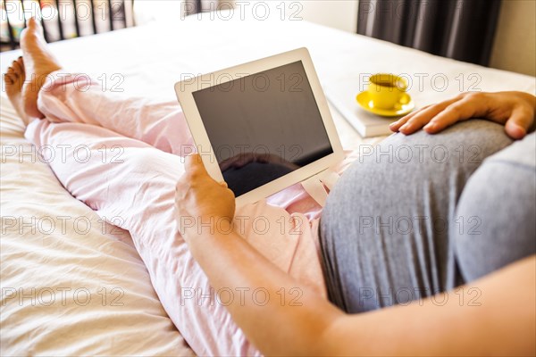 Pregnant Caucasian woman using digital tablet in bed