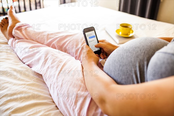 Pregnant Caucasian woman using cell phone in bed