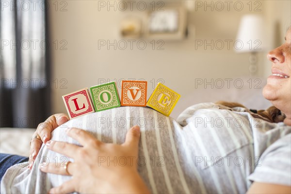 Pregnant Caucasian woman balancing wooden blocks on her stomach in bed