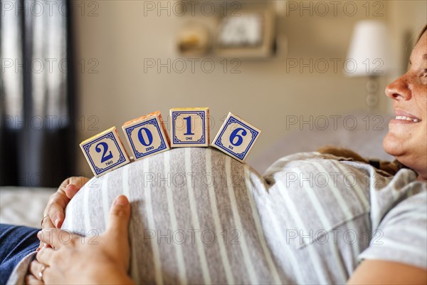 Pregnant Caucasian woman balancing wooden blocks on her stomach in bed