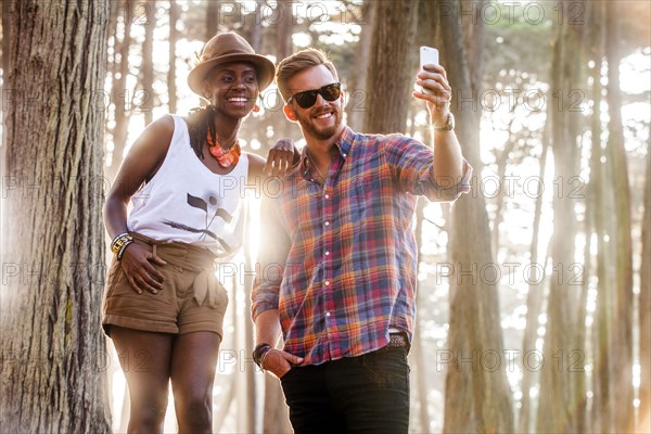 Couple taking cell phone picture in sunny forest