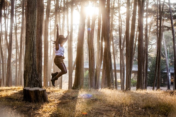 Black woman jumping from stump in sunny forest