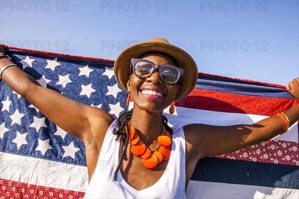 Black woman holding American flag under blue sky