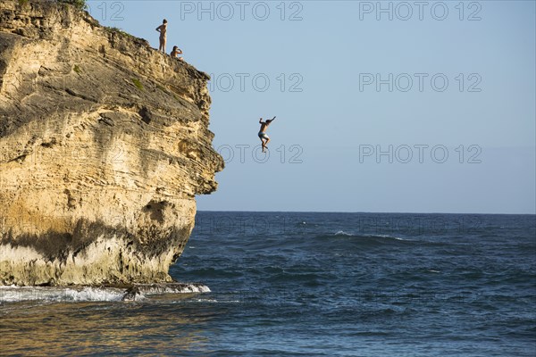 Divers jumping off cliff into ocean