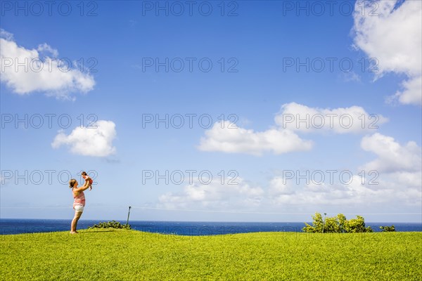 Mother and child playing in grass field under blue sky