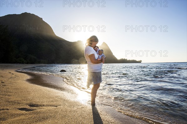 Caucasian mother holding baby in waves on beach