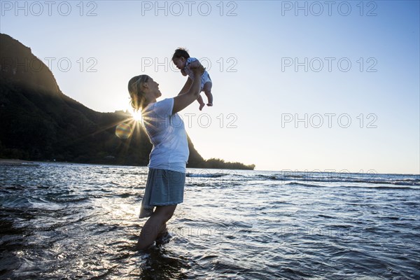 Caucasian mother holding baby in ocean on beach