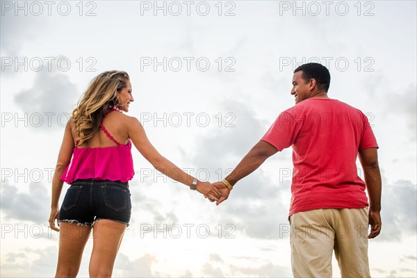 Low angle view of couple holding hands under cloudy sky