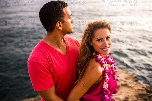 Smiling couple hugging on rocks over ocean