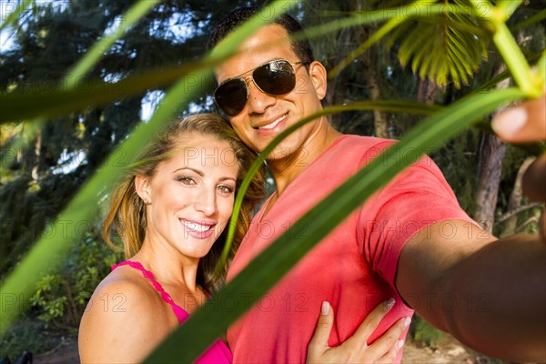 Smiling couple hugging behind palm frond leaves