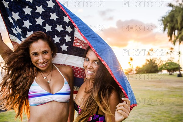 Women standing under American flag quilt at sunset