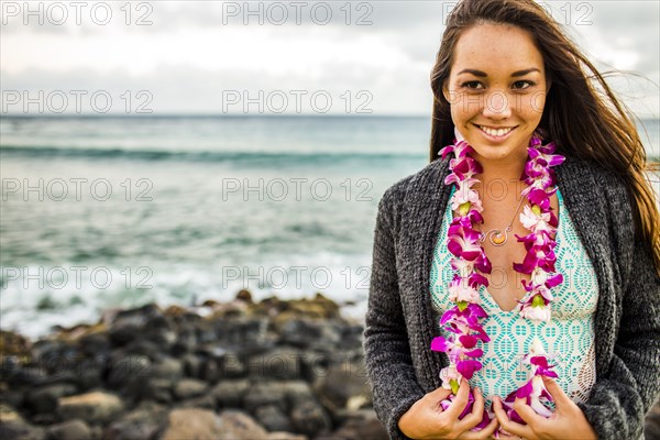 Pacific Islander woman wearing flower lei near rocky beach