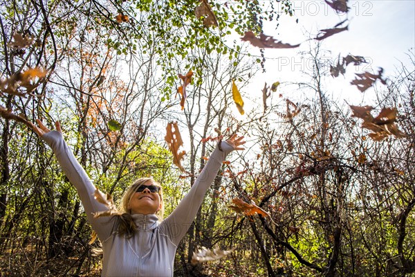 Caucasian woman throwing autumn leaves in forest