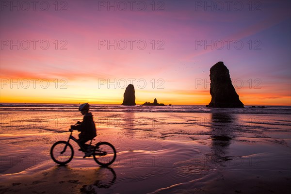 Silhouette of Caucasian girl biking near rock formations on Cannon Beach